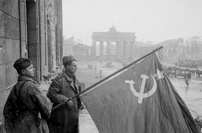 Советские военные — рядовой и лейтенант — со знаменем в Берлине на фоне Бранденбургских ворот, 1945 г.