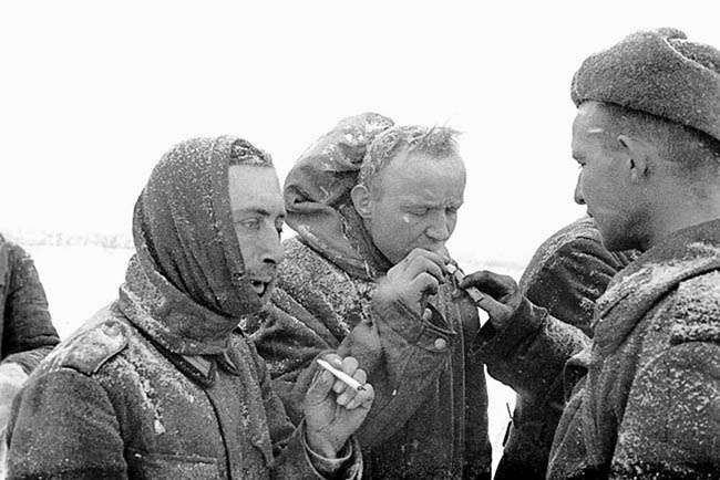 Советский боец дает прикурить пленным немцам.